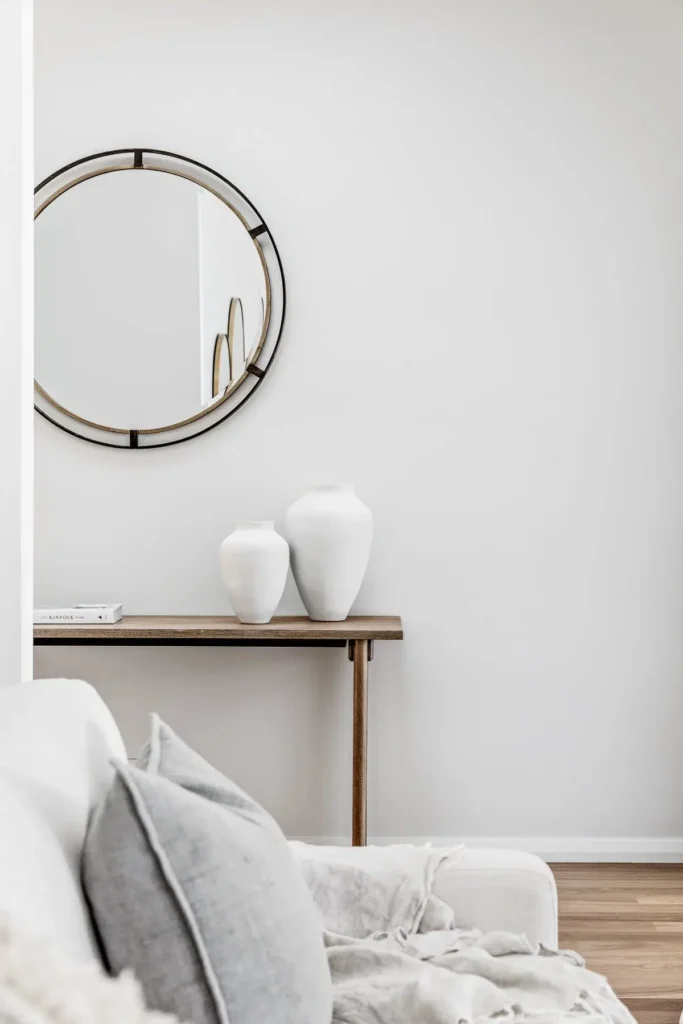 Airbnb styling idea: a round mirror above a timber console with white ceramic vases