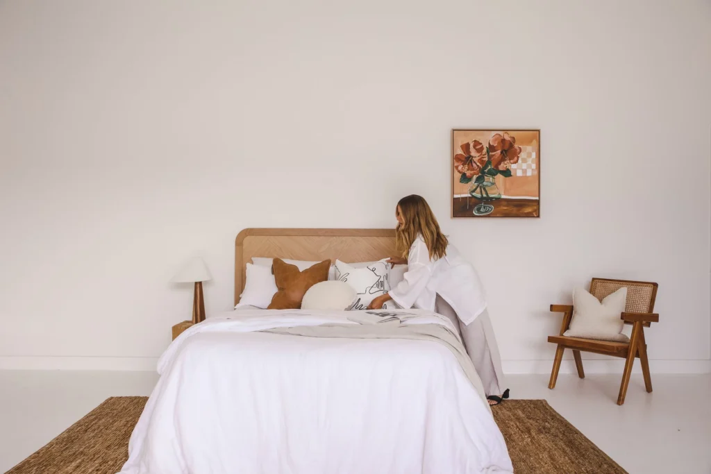 Styling a holiday rental bedroom with layered white bedding, a timber bedhead and artwork