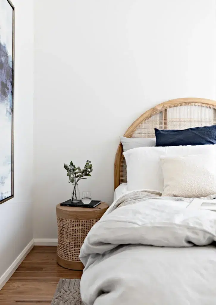 Holiday rental styling in a bedroom with a rattan bedhead, linen bedding and a woven bedside table