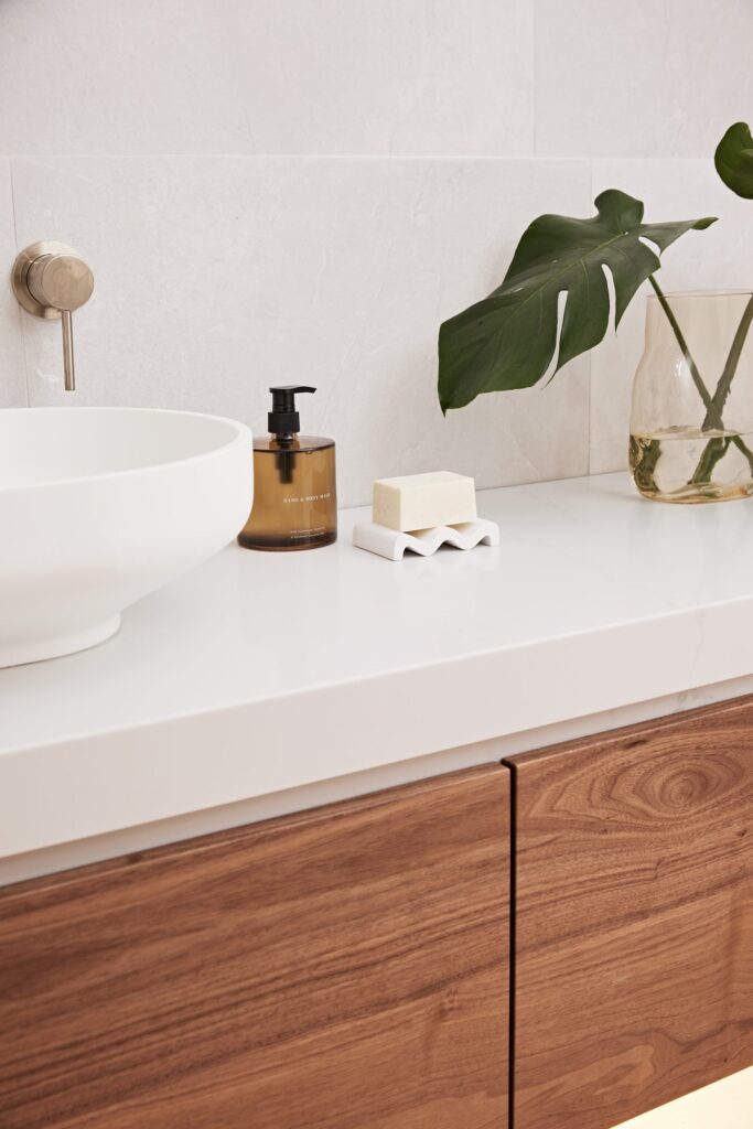 Close-up of a styled bathroom vanity with a timber cabinet, stone benchtop and greenery